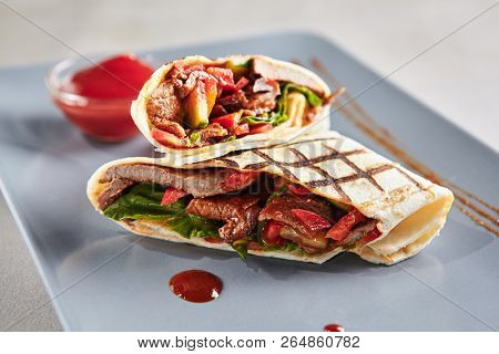 Barbeque Meat Shaverma or Doner Kebab with Vegetables on Blue Plate. Thin Tortilla Rolls Stuffed with Sliced Fried Beef, Pork and Chicken Fillet Cucumber, Tomato, Sauce, Paprika and Greens