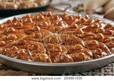 Beautiful Serving Homemade Baklava in a Round Metal Tray on Vintage Traditional Tablecloth. Sweet Turkish Style Brown Glazed Pastries Baklawa with Walnut, Nuts, Sugar, Pistachio and Honey Close Up