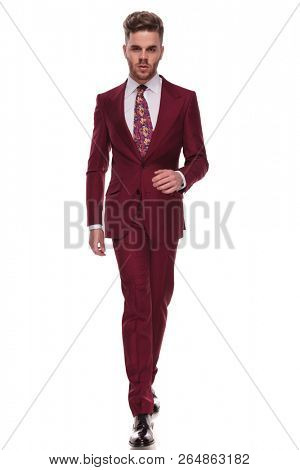 confident man with beard walking forward on white background while wearing grena suit