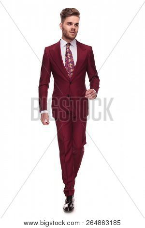 handsome man in grena suit steps on white background and looks up to side, full length picture