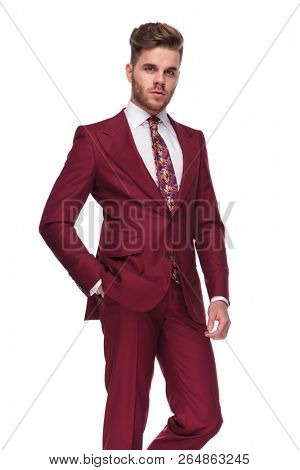 portrait of handsome and relaxed young man in grena suit standing on white background with a hand in pocket