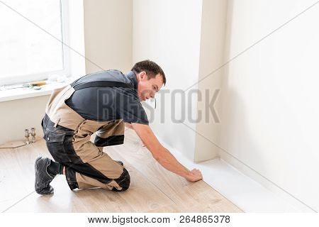 Male Worker Installing New Wooden Laminate Flooring On A Warm Film Foil Floor. Infrared Floor Heatin