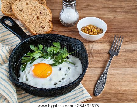On A Wooden Background There Is A Cast-iron Pan With Scrambled Eggs With Greens, Salt, Grain Bread, 