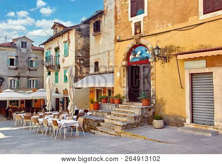 Lovran, Croatia. Central area of ancient old town with vintage buildings and cosy street cafes and restaurants. Sunny summer day. Urban landscape of historical centre.
