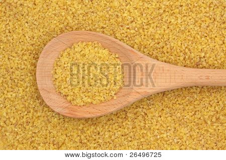 Blé bulgur dans une cuillère en bois et en formant un fond.