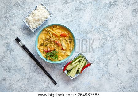 Traditional Chinese or Thai chicken yellow curry with vegetables served with steamed rice cucomber and hot chilli pepper on side. Top view with copy space on stone background.