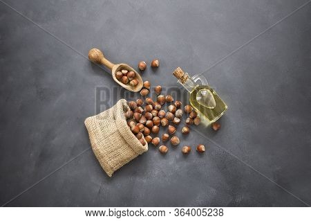 Hazelnuts, Filbert In Burlap Sack And Hazelnut Oil In Glass Of Bottle On Rustic Backdrop. Heap Or St