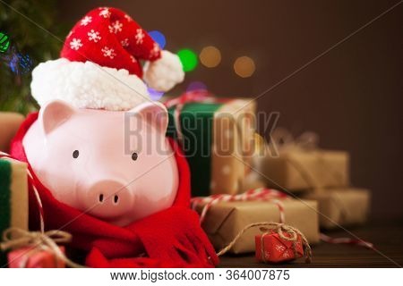 Piggy Bank In Santa Claus Christmas Hat. Gift Boxes, Spruce Branches, And A Garland.