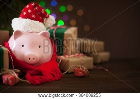 Piggy Bank In Santa Claus Christmas Hat. Gift Boxes, Spruce Branches, And A Garland.
