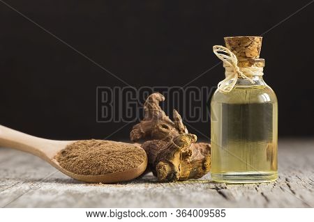 Glass Bottle Of Galangal Essential Oil, Root And Galanga Powder In Wooden Spoon On Rustic Table. Hea