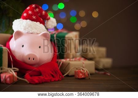 Piggy Bank In Santa Claus Christmas Hat. Gift Boxes, Spruce Branches, And A Garland.