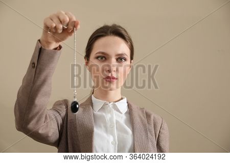Psychotherapist With Pendulum On Beige Background. Hypnotherapy Session