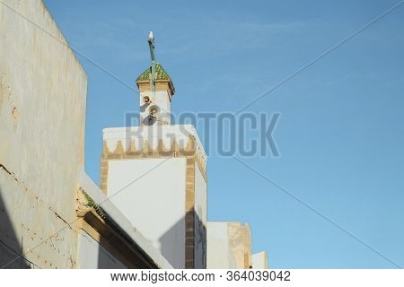 Muslim White Minaret Tower For Calling Prayer To Pray At Local Mosque Against Blue Sky Background