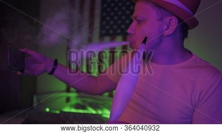 Hipster Smokes A Hookah While Taking A Selfie With A Mobile Phone, Man On Self-isolation In A Home I