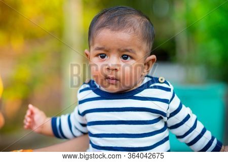 A Baby Boy Looking And Smiling. Dressed Are White And Navy Blue Striped Dress. Baby Candid Shoot. Ba