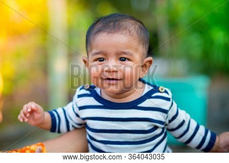 A Baby Boy Looking And Smiling. Dressed Are White And Navy Blue Striped Dress. Baby Candid Shoot. Ba