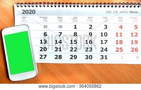 A Mobile Phone With A Green Screen And A Copy Of Space Is On The Calendar Sheet For July 2020