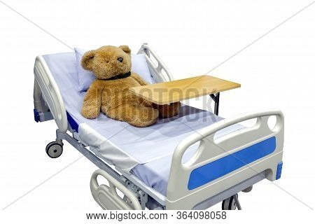 Brown Teddy Bear Lying Sick In Bed With Overbed Table On Body, Isolated On White Background, Medical