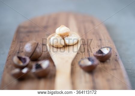 Macadamia Lying In A Wooden Spoon. Nuts Peeled From Nutshell On Oak Board On Grey Table Background. 