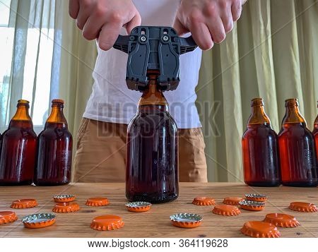 Craft Beer Brewing At Home, Man Closes Brown Glass Beer Bottles With Plastic Capper On Wooden Table 