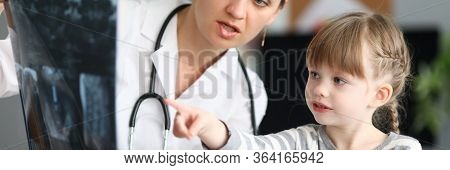 Portrait Of Experienced Focused Pediatrician Showing Skiagram Of Serious Sick Child. Little Girl Poi