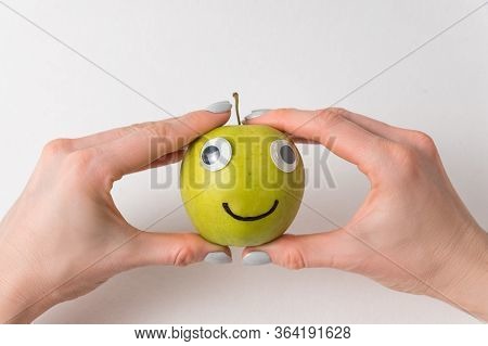 Hands Holding Cute Little Apple With Googly Eyes And Drawn Smile. Apple Haracter On White Background