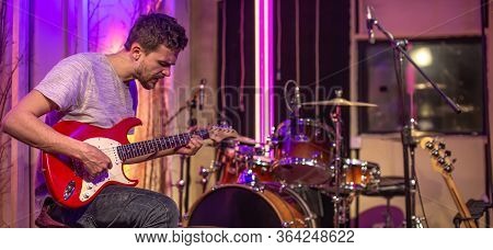 A Man Plays An Electric Guitar In A Recording Studio. A Rehearsal Room For Musicians With A Drum Kit