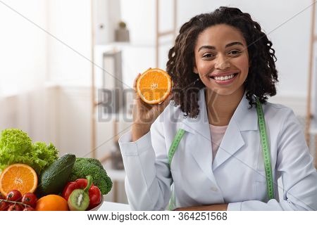 Vitamin C For Immunity. Cheerful African Woman Dietologist Holding Orange Half, Recommending Frresh 