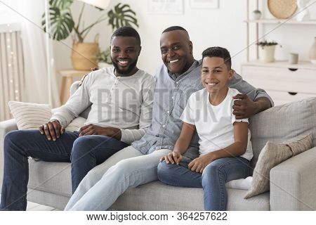 Africam American Grandfather With Son And Grandson Relaxing Together At Home, Embracing On Sofa, Loo
