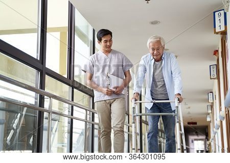 Young Asian Physical Therapist Working With Senior Man On Walking Using A Walker