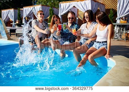Group Of Friends Having Fun At Poolside Party Clinking Glasses With Fresh Cocktails Splashing Water 