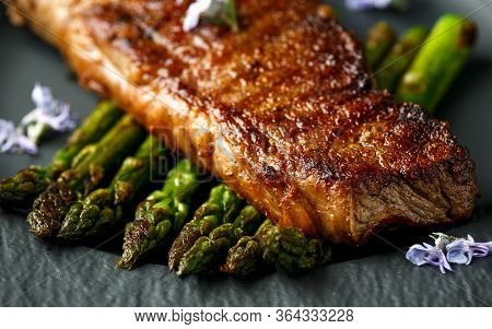 Grilled Sirloin Beef Steak On Fried Asparagus Served On Black Slate Plate With Rosemary Flowers