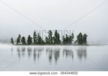 Fog-covered Trees On The Shore Of A Mountain Lake Are Reflected In The Water In The Ulagansky Distri