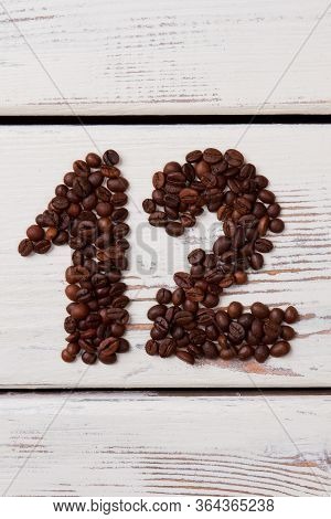 Coffee Beans In A Shape Of Number Twelve On White Surface. Brown Roasted Seeds On Wooden Planks Form