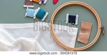 Embroidery Tools On Green Background With Wooden Embroidery Hoop, Needles, Needle Threader And Color