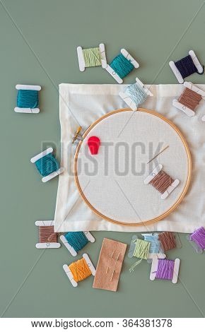Embroidery tools on green background with wooden embroidery hoop, needles, needle threader and color