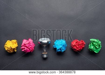 Lightbulb And Crumpled Colorful Paper Balls On Black Background. Successful Solution Of Problem. Ide