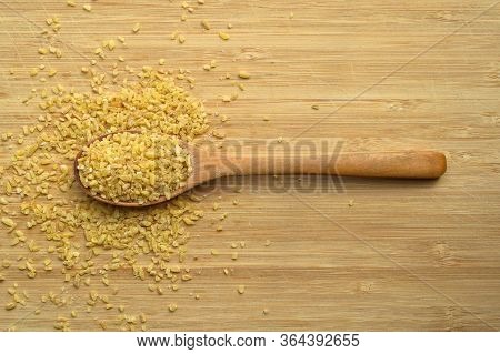 Dry Cracked Wheat Daliya Grains In Wooden Spoon, On Bamboo Cutting Board