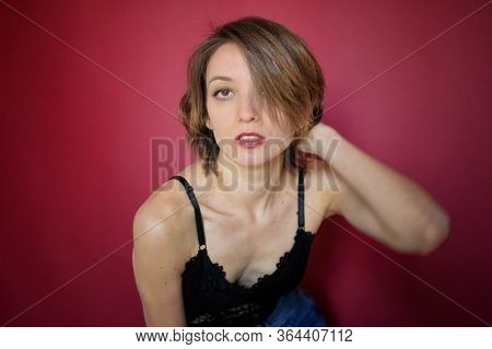 Young Woman With Short Hair Dressed In Black Lace Bustier And Blue Jeans Is Posing In The Studio On 