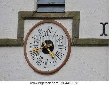 Ancient Clock With Roman Numerals And Gold Hands Integrated In The Wall Of St. Peter And Paul Church