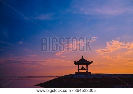 Silhouette Of A Man Sitting In A Gazebo On The Beach At Dawn On Sanur Beach, Bali, Indonesia. A Man 