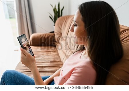 Portrait Of Young Girl With A Smartphone, She Talks Online With Friend While Sitting On The Sofa At 