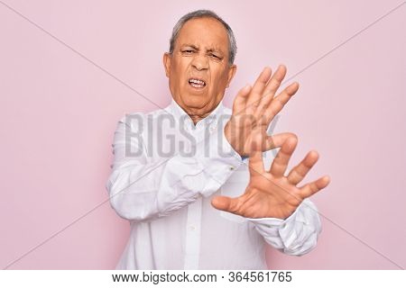 Senior handsome grey-haired man wearing elegant shirt over isolated pink background disgusted expression, displeased and fearful doing disgust face because aversion reaction. With hands raised