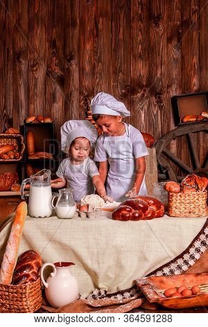 Cheerful Kids Playing Chefs And Hats Play The Role Of Baker.
The Table Is Full Of Clutter. The Mood 