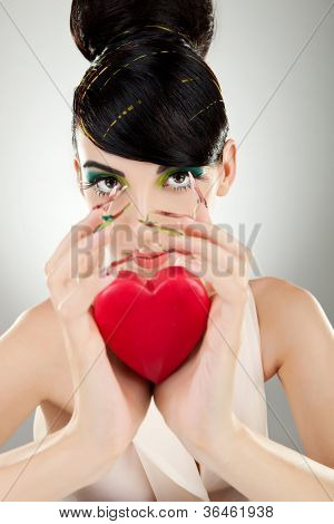 Aantrekkelijke jonge vrouw model met excentriek make-up en manicure houden een hart