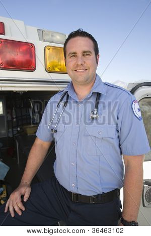 Portrait of a happy middle aged EMT doctor standing with ambulance in the background