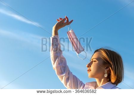 Happy Woman Takes Off Medical Protective Mask Holds It On Her Finger On Blue Sky Background, Enjoys 