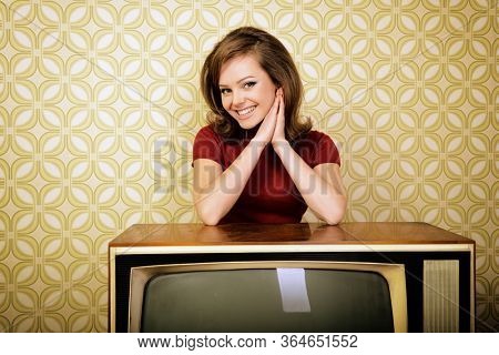 Young charming woman staing at room with vintage wallpaper and retro TV set, retro stylization 60-70s, image toned