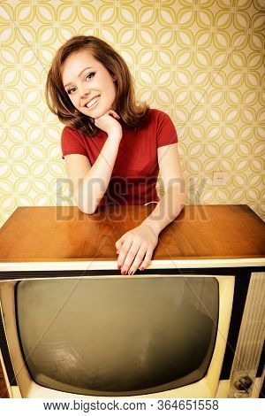 Young charming woman staing at room with vintage wallpaper and retro TV set, retro stylization 60-70s, image toned. Self isolation, quarantine, stay at home