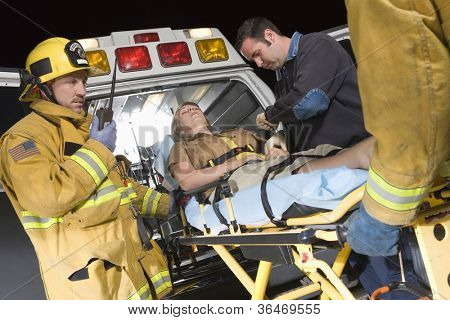 Emergency service professionals carrying patient on stretcher in ambulance